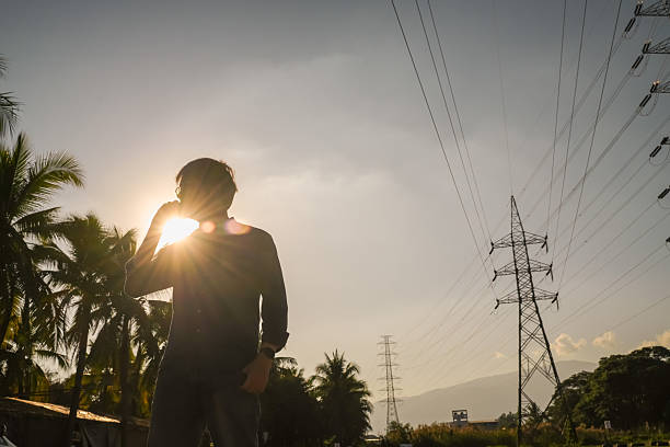 Silhouette of Engineer Inspecting High Voltage Power Lines at Sunset