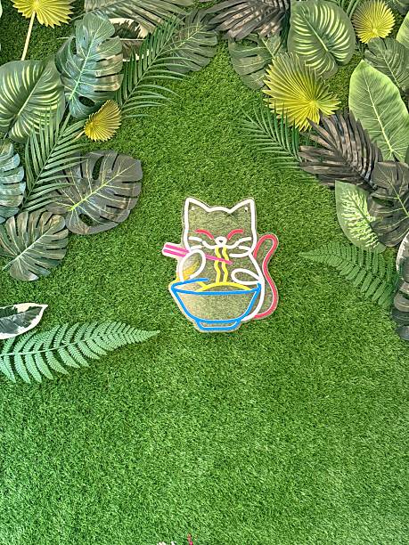 Neon cat sign on green grass surrounded by tropical leaves, suitable for background use