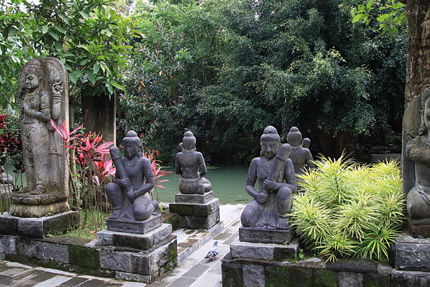 Ancient stone statues stand serenely in a lush garden pond in Indonesia, creating a peaceful and spiritual atmosphere for visitors and worshippers alike.
