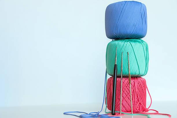 Colorful yarn skeins stacked vertically with crochet hooks leaning against them on a light pastel background. Minimalist composition suitable for knitting, crochet, handmade crafts, DIY projects, textile design, and creative hobbies.