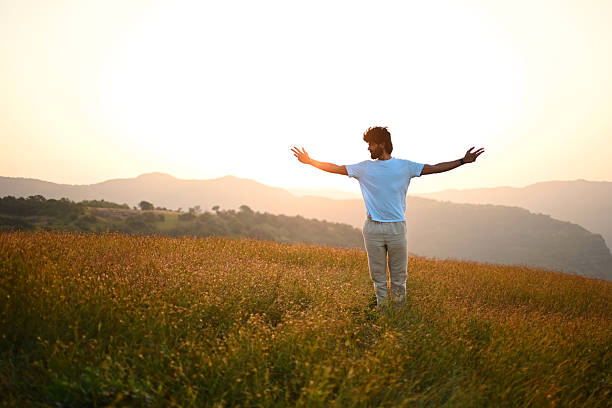 istock Man Standing with Open Arms at Sunrise in Mountain Meadow 2252216841