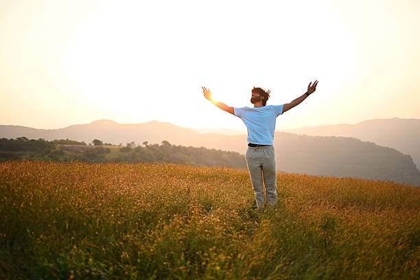 istock Man Standing with Open Arms at Sunrise in Mountain Meadow 2252216846