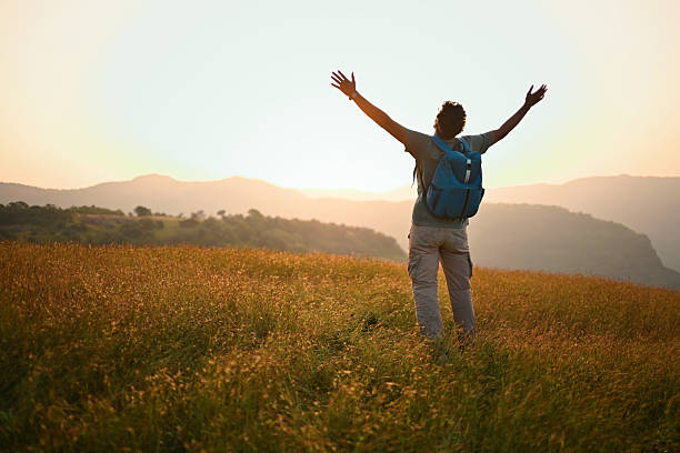 istock Man Standing in Meadow at Sunrise with Arms Open Toward Mountains 2252216849