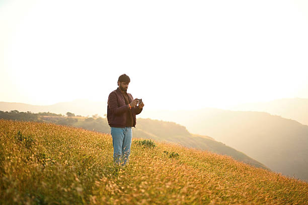 istock Man Using Smartphone on Grassy Hill at Golden Hour 2252217571