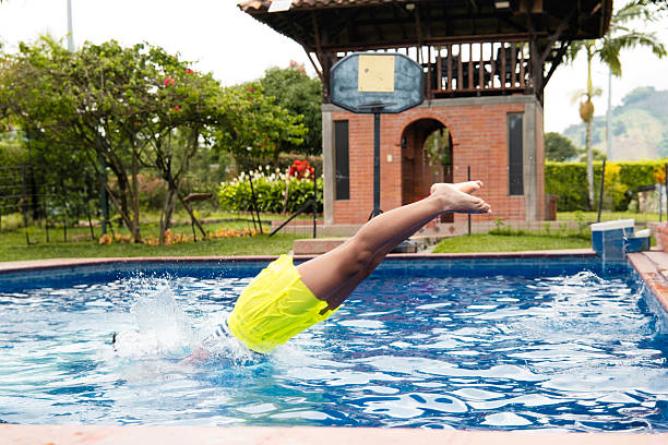 Person wearing yellow swim shorts diving headfirst into a swimming pool on a summer day, creating a large splash