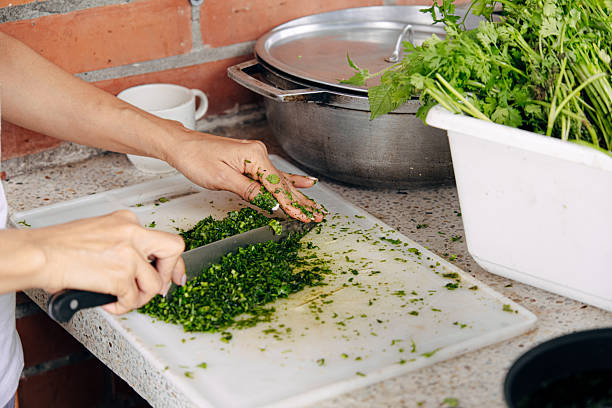 Person's hands chopping fresh green cilantro on a white cutting board, preparing ingredients for a meal in the kitchen