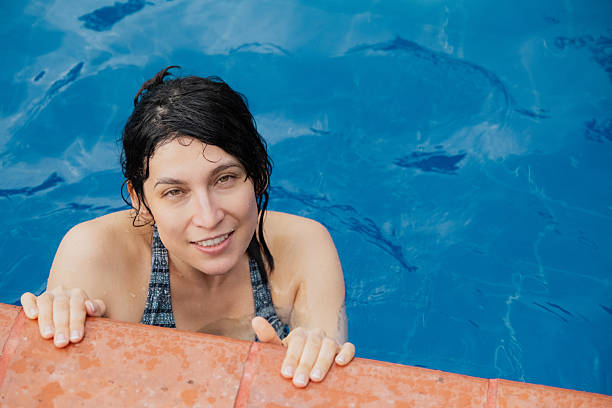 Woman smiling and looking at the camera, relaxing in a swimming pool on a sunny day during her summer vacation