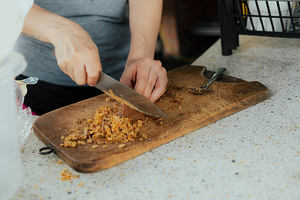 Person's hands chopping food ingredients on a wooden cutting board, preparing a meal in a home kitchen