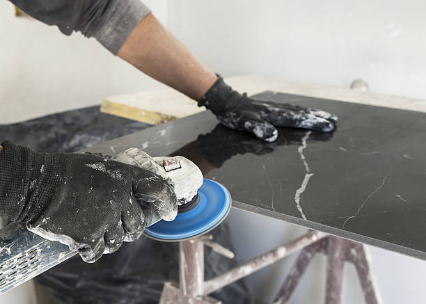 istock Craftman in grey shirt grinds black ceramic tile using an sand grinder. Handy men at work, hands closeup 2252218630