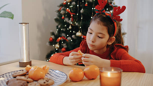 Young girl preparing and enjoying tangerines during a festive holiday gathering by a decorated Christmas tree