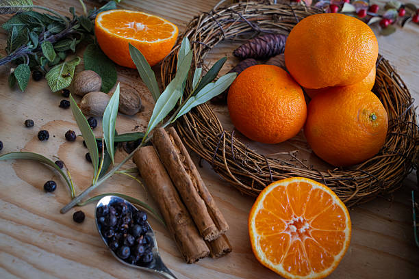 Hands making holding ragrant pomander balls handmade from tangerines and cloves. Flat lay on off white textile tablecloth with aromatic wintertime green eucalyptus twigs.