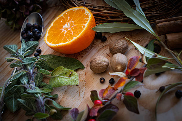 A close-up still life composition features several one halved tangerine revealing juicy segments, centred within a woven twig wreath base. The arrangement is surrounded by evergreen branches, possibly fir (Abies spp.), and clusters of red cotoneaster berries , with green leaves adding texture. The vibrant orange fruits contrast against the deep green foliage and bright red berries, creating a warm, festive mood suitable for winter holidays. Set indoors on a light wooden surface, the image evokes seasonal abundance and natural beauty. Ideal for commercial uses such as holiday recipe illustrations, Christmas greeting cards, seasonal food packaging, winter-themed advertisements, or editorial content in lifestyle magazines focusing on fresh produce and festive décor.