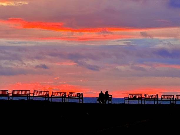 Two people sitting on a public bench watching the sun rise at Tynemouth