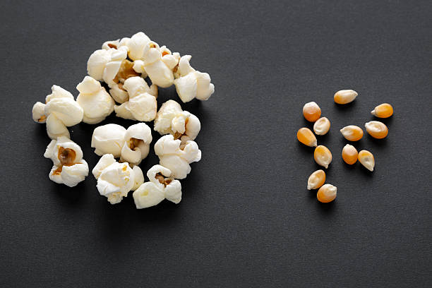 Wooden spoon with popped corn kernels placed on a raw seeds background.