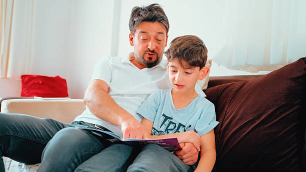 istock Father Helping His Son Read a Book on the Sofa at Home 2252233223