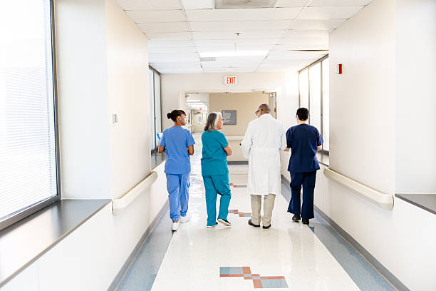 Three medical professionals, including a doctor, walk and talk in a bright hospital hallway, likely discussing patient care or medical procedures.