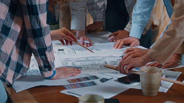 istock Creative casual informal business team group talking discuss building papers blueprint plan writing drawing communicate together five people diversity coworkers architects in office engineers talk 2252234554