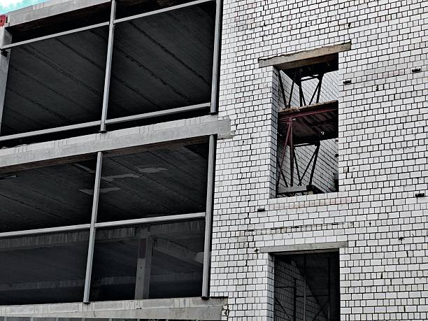 Close-Up of Unfinished Brick Building Facade. Detailed view of partially built white brick wall with concrete elements and window openings during construction.