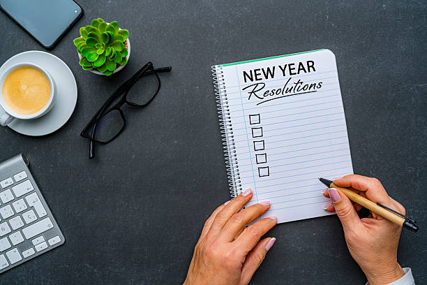 istock Person and checklist in minimal workspace desk with New Year resolution notebook. Goals, resolutions, strategy, plan, action, checklist for the coming year. Coffee cup, plant, eyeglasses and mobile phone. 2252238398