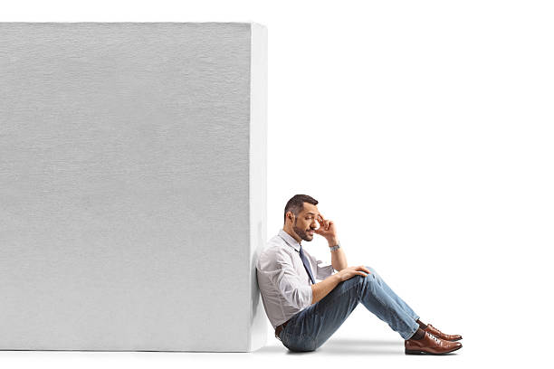 istock Disappointed man sitting with back against a wall 2252248290