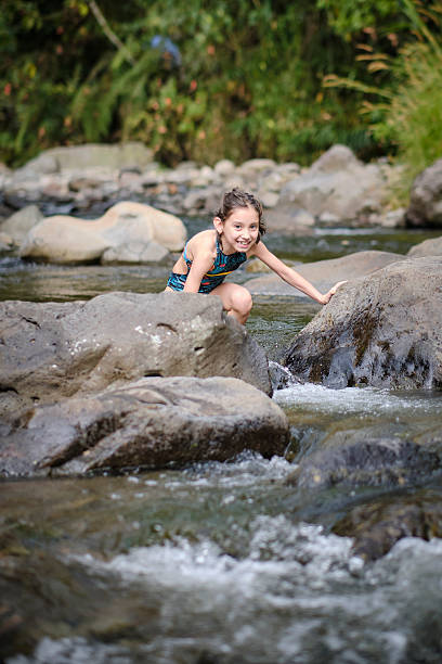 Young child with a happy expression playing in a natural river, stepping on rocks and enjoying the outdoors
