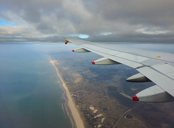 istock Airplane wing flying above coastline, ocean, and clouds 2252256104