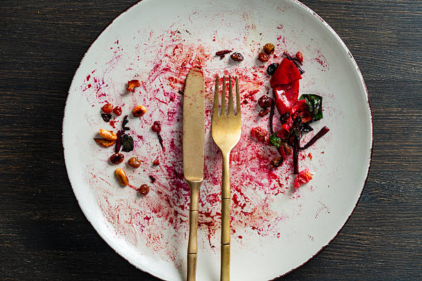 Dirty plate, fork and knife after eating on a wooden table, closeup, top view. End of meal
