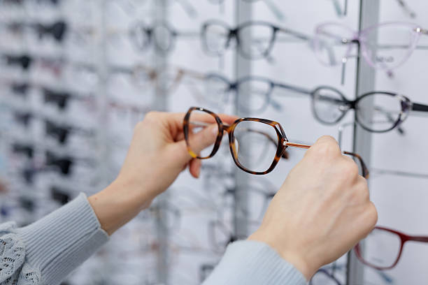 istock Hands comparing tortoiseshell eyeglasses in optician store showroom wall display 2252262780