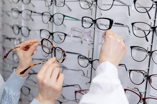 istock Optician helping customer compare eyeglass frames on display wall in optical store close up 2252262781