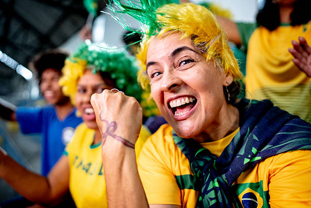 istock Joyful Brazilian fan cheering taking a selfie or filming during sporting event - camera point of view 2252265000