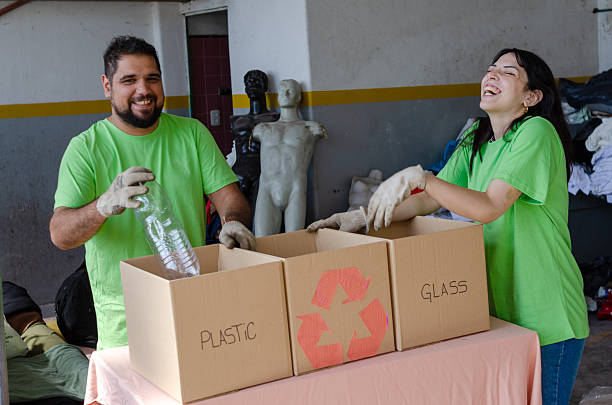 An interracial couple brings trash to be recycled at the recycling center. Two other people, a mother and daughter, are in the background.