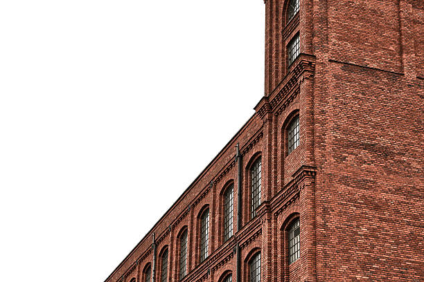 Red brick industrial building facade with tall windows against a white sky. Minimalist urban architecture background with large copy space for real estate, construction and business concepts.