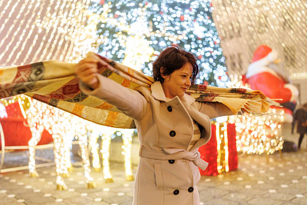 Happy mature woman spinning by Christmas tree and lights during the evening in the city of Timisoara, Romania.