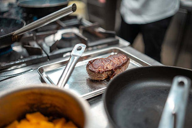 restaurant kitchen, steaks are fried on a grill pan, meat is beef, pork, lamb, splashes of oil are flying, smoke is coming, the work of the cooks.