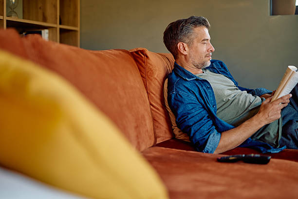 istock Man relaxing reading book on couch at home 2252277029