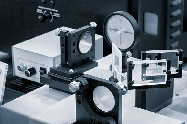 Optical equipment including telescope and lenses are displayed on a table in a laboratory. Optics and photonics concept science experiment with laser background