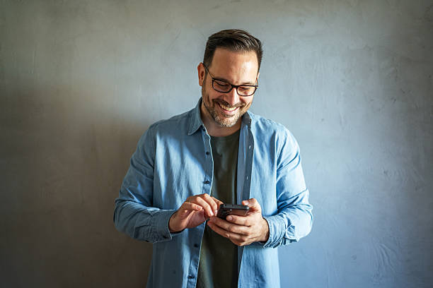 istock Happy man in eyeglasses holding a phone looking away 2252278484