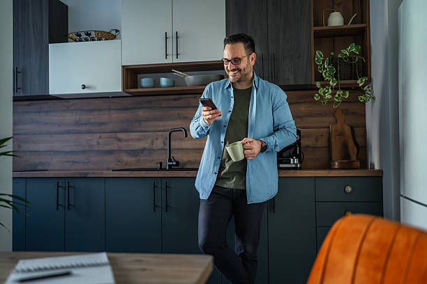 istock Man drinking coffee and checking phone in home office kitchen 2252278628