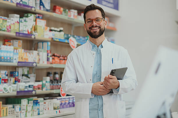 istock Smiling male pharmacist standing in white coat holding tablet 2252284925