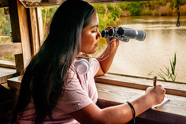 istock Young woman bird watching and writing notes by lake 2252286749