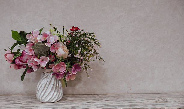 Elegant floral arrangement with pink and pastel flowers in a ceramic vase placed on a wooden surface against a soft neutral background. Minimalist home decor, romantic mood, natural light, copy space for text, interior styling and floral design concept