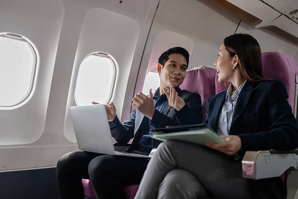 istock Two Asian business professionals smiling and discussing ideas during a flight, sitting next to each other in an airplane cabin. The man gestures confidently while the woman listens attentively. 2252293142