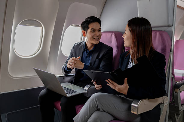 istock Asian businesspeople discussing work while flying on a plane. The man gestures as he explains something, while the woman listens holding a folder and pen, showing in-flight collaboration. 2252293186