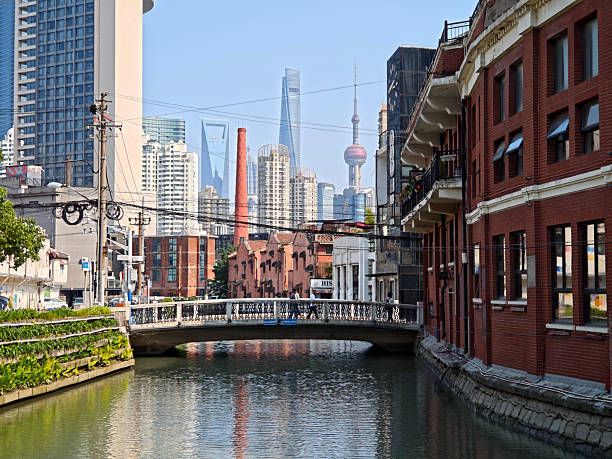 People crossing a canal bridge with the futuristic Lujiazui finance and trade zone skyline in the distance, Hongkou district, Shanghai, China