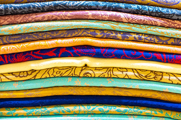 Detailed photo of stacked decorative fabrics featuring vivid colors, woven patterns, and ornamental designs. The layered textiles create a rich background suitable for fashion, interior design, crafts, ethnic style, handmade products, and cultural or luxury branding concepts.