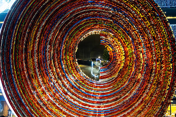High-impact abstract image of a vibrant spiral tunnel art installation composed of colorful layered materials. The circular motion, light reflections, and night setting create a dynamic futuristic background perfect for art, design, innovation, and creativity themes.