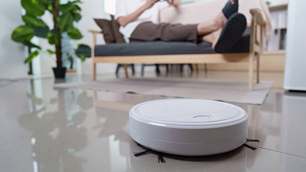 istock Home Automation. Robotic vacuum cleaner cleaning floor while user relaxes on couch. 2252303157