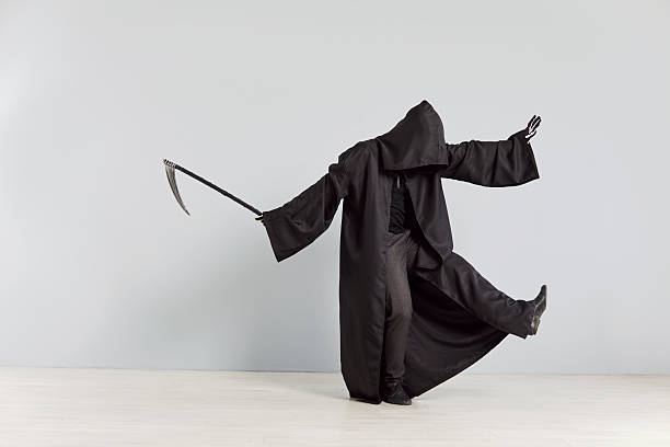 Grim reaper, with a devilish mask and skeleton attire, dances while holding a scythe against a grey background. This eerie death figure embodies Halloween spooky spirit with a chilling performance.