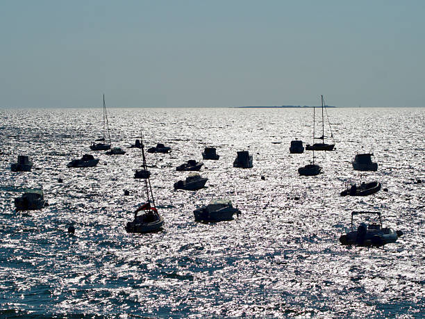Horizontal seascape photo of boats in silhouette moored on the sea near the beach at Mesquer, Brittany in Summer