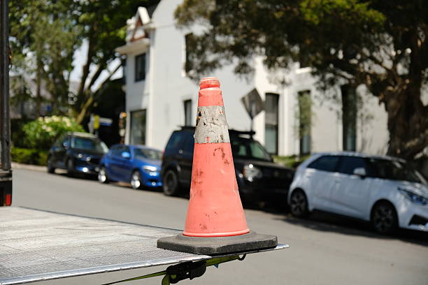 Old faded orange traffic cone on a truck loading platform on a tree-lined street.